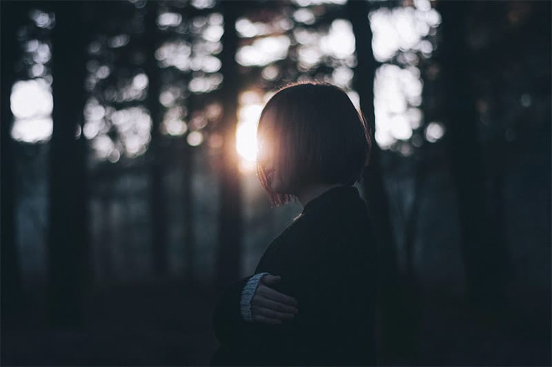 Sad woman in forest, sunlight behind her