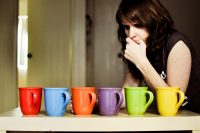 Woman thinking, having to choose between different colored cups
